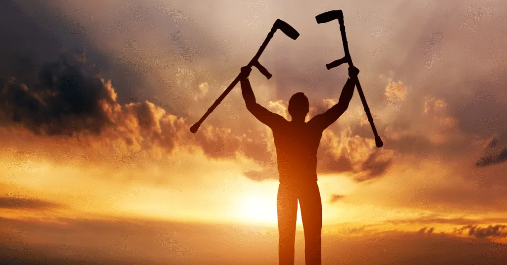 Persona levantando muletas al amanecer, símbolo de recuperación y retorno laboral.