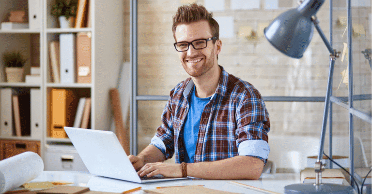 Trabajador independiente sonriente utilizando su computador portátil mientras trabaja desde casa en Colombia.