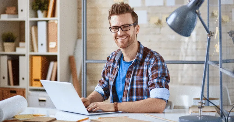 Trabajador independiente sonriente utilizando su computador portátil mientras trabaja desde casa en Colombia.