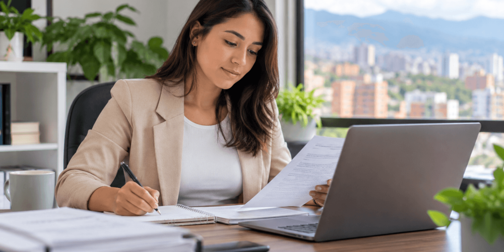 Trabajadora independiente administrativa revisa documentos y realiza gestión desde un computador en un entorno de oficina.