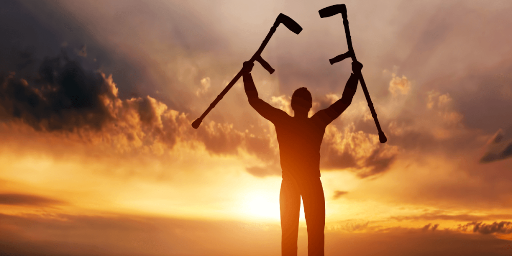 Persona levantando muletas al amanecer, símbolo de recuperación y retorno laboral.