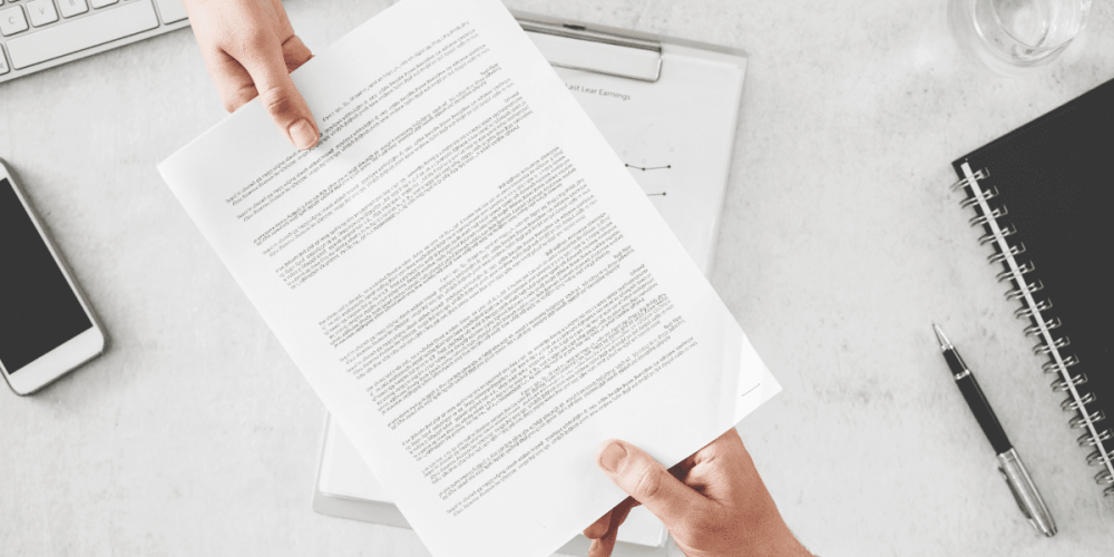 Persona entregando un certificado ocupacional firmado en un entorno de oficina, con celular y herramientas de trabajo sobre el escritorio.