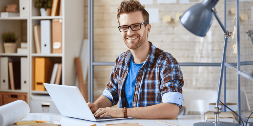 trabajador-independiente-certificado-ocupacional-colombia. Trabajador independiente sonriente utilizando su computador portátil mientras trabaja desde casa en Colombia.