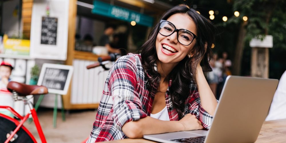 Debonair white girl in casual shirt posing on street background with computer. Outdoor portrait of enthusiastic female student using laptop.