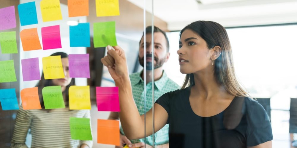 Female young manager discussing over adhesive note with coworkers in office meeting