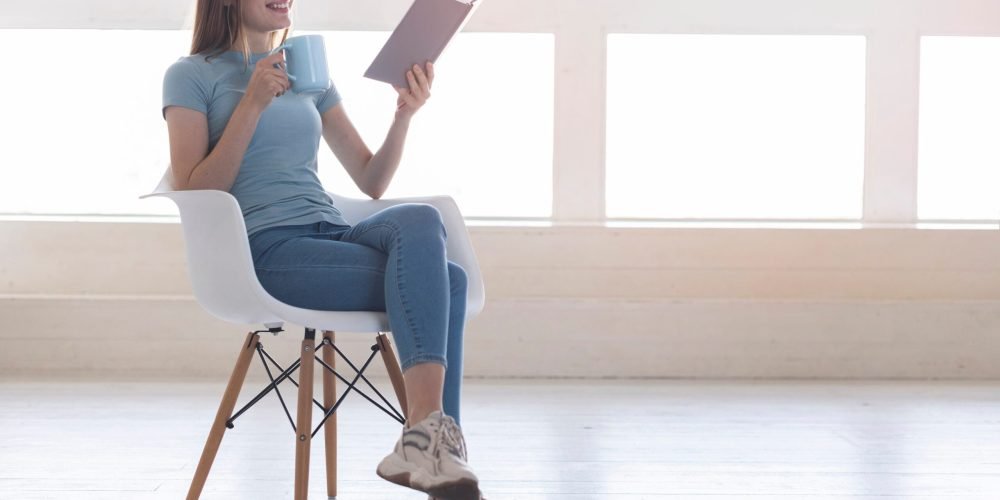 long-shot-woman-sitting-on-chair-while-reading-book